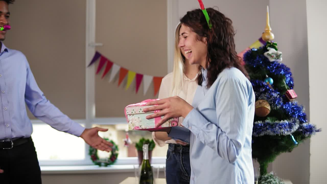 젊은 매력적인 여성이 여성 동료에 의해 눈을 감고 서 있는 동안 남성 직원은 그녀를 놀라게 하고