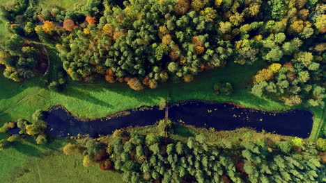 Bird's-eye-view-of-narrow-winding-lake-surrounded-by-green-vegetation-on-sunny-day-in-the-countryside