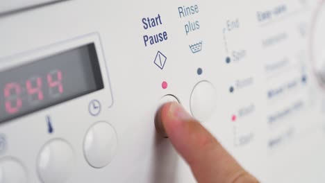 close up shot of slow motion finger pressing start pause button on washing machine dial rinse clothing cleaning laundry detergent household 4k