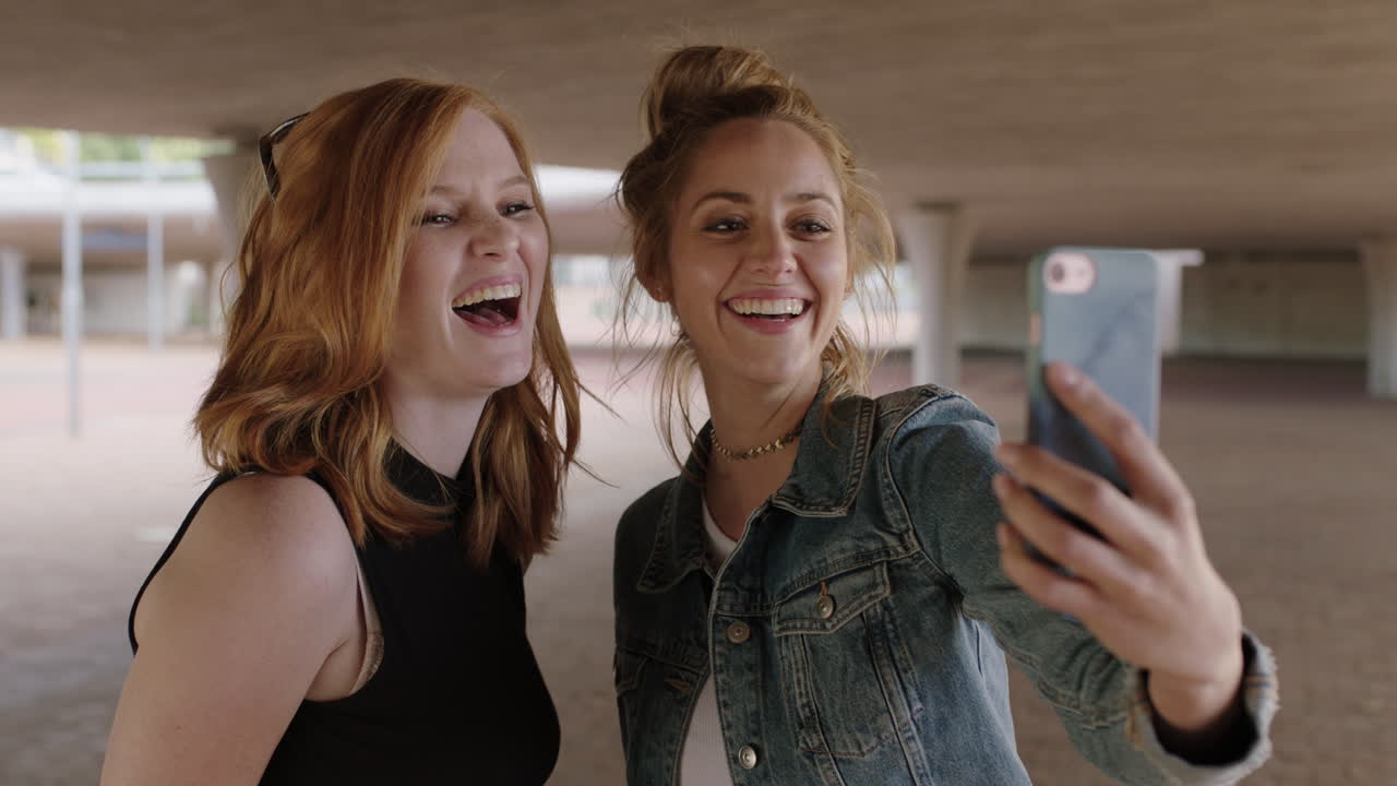 To smukke unge kvinder bruger smartphone, poserer til selfie-foto og laver sjove, glade ansigter.