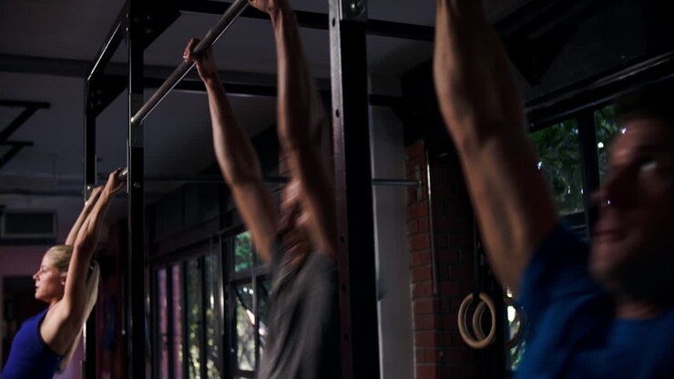 Three people doing chin up exercises on a pull up bar in a gym