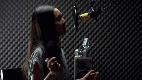 mujer adolescente asiática envuelta en cabello largo negro canta una canción en voz alta con sonido potente sobre condensador de micrófono colgante y equipo