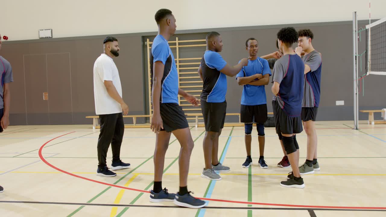 Diverse Teamkollegen versammeln sich in Netznähe, während ein afroamerikanischer Trainer von links hereinkommt und eine Strategie andeutet.