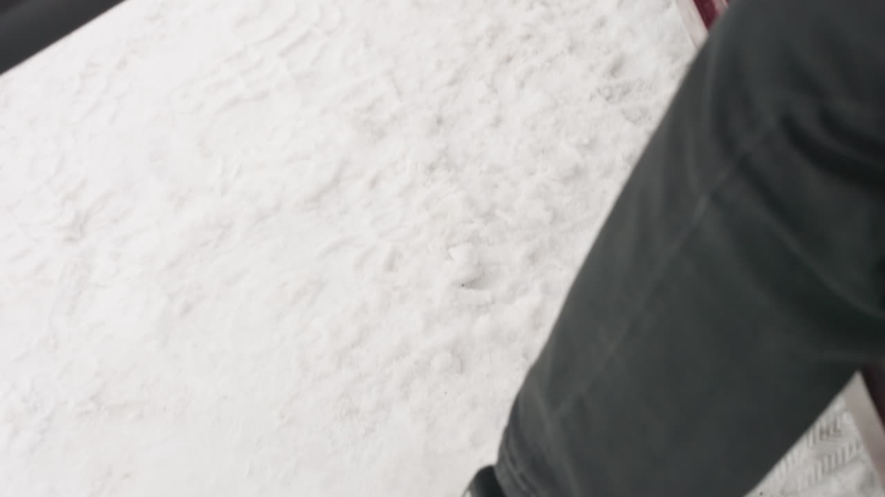 interior view of open car door as lower body exits vehicle and foot makes contact with snowy ground outside frame reveals textured fabric panel, door edge, and metal doorstep