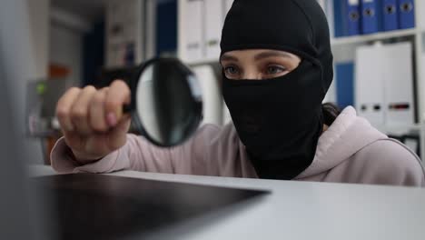 hombre en balaclava mirando la pantalla del portátil con lupa película 4k