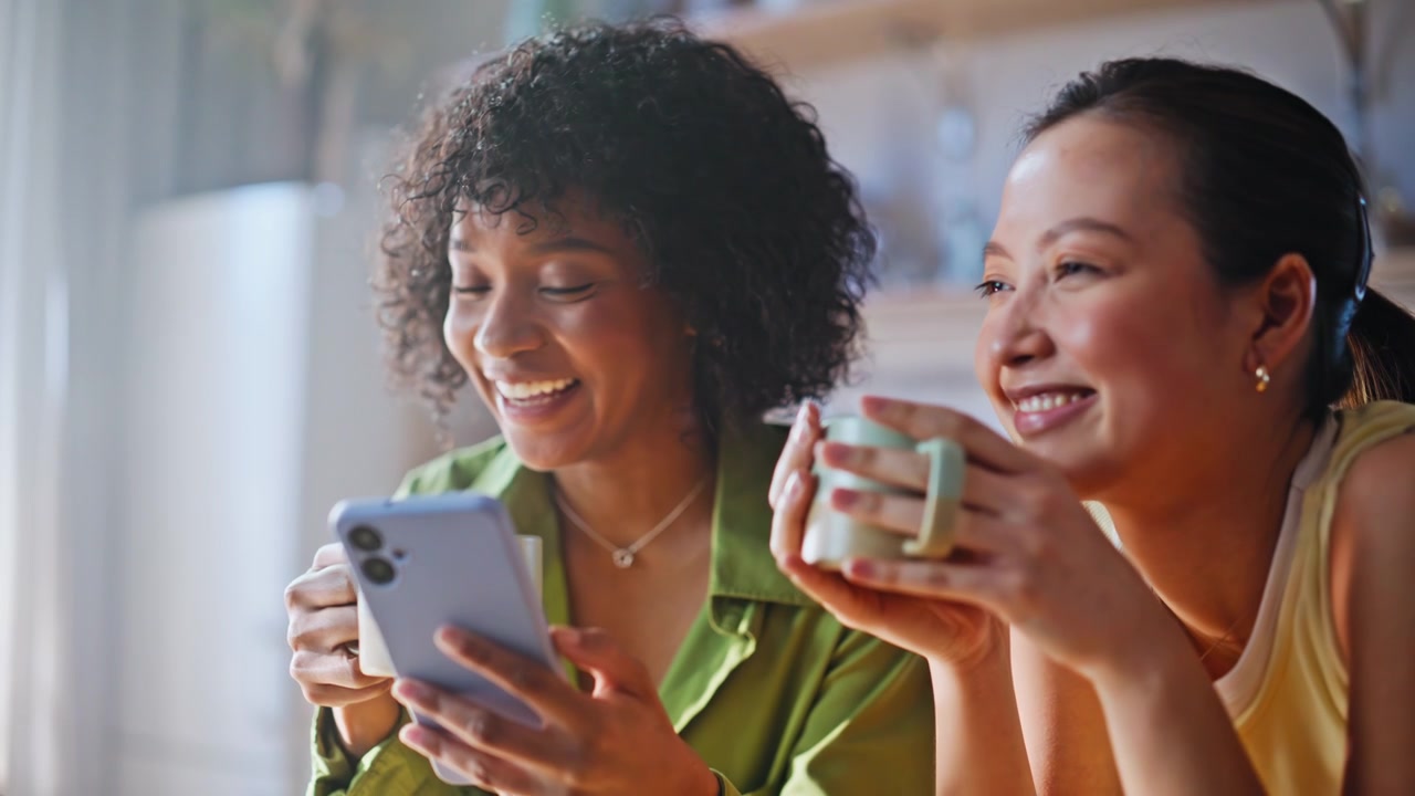 Multiracial friends laughing phone. Closeup women drinking coffee home kitchen.