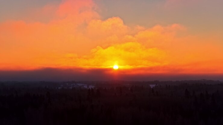 Stella solare che brilla sopra uno strato di nuvole e una campagna innevata in inverno, con nuvole giallo-arancio gonfie.
