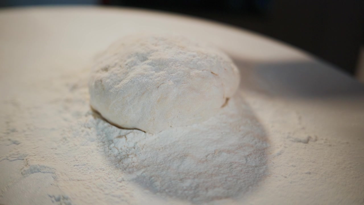 Hands knead soft dough on floured surface. Flour dusts around dough. Person focused on shaping dough. Ideal for baking, cooking, or food preparation content