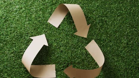 primer plano del símbolo de reciclaje de flechas de papel sobre fondo de hierba, con espacio para copiar