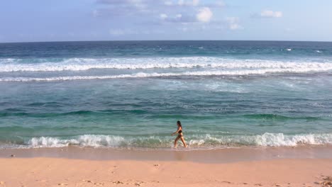 Aerial-panning-left-tracking-woman-walking-along-the-shore-of-the-beach-at-sunset