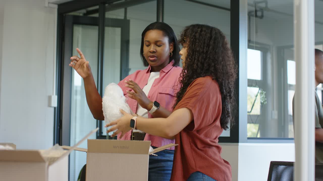 African American coworkers two women packing bubble wrap into boxes at office, preparing for move