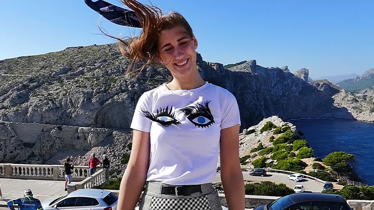 Slow motion (120fps): young lady smiling at the mountainous shore during the windy day in Mallorca island, Spain