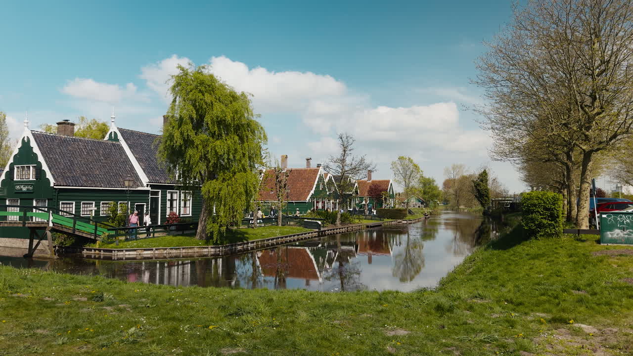 Tradizionali case olandesi in legno verde che si riflettono in un tranquillo canale nel villaggio storico di Zaanse Schans, Paesi Bassi, in una soleggiata giornata di primavera
