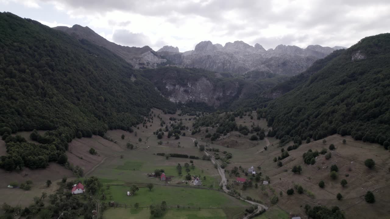 video drone del avion frontal avanzando sobre el valle de lepushë sobre el rio lëpusha, el sh20 en albania, se pueden ver casitas del pueblo, un cielo algo nublado y el rio seco