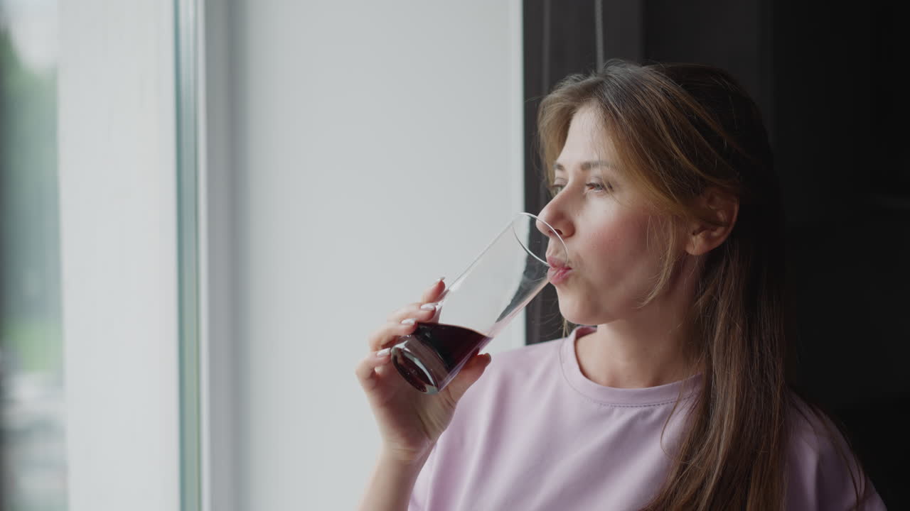 young white lady standing near glass window sipping wine relaxed serene thoughtful expression natural daylight gently illuminating face long hair