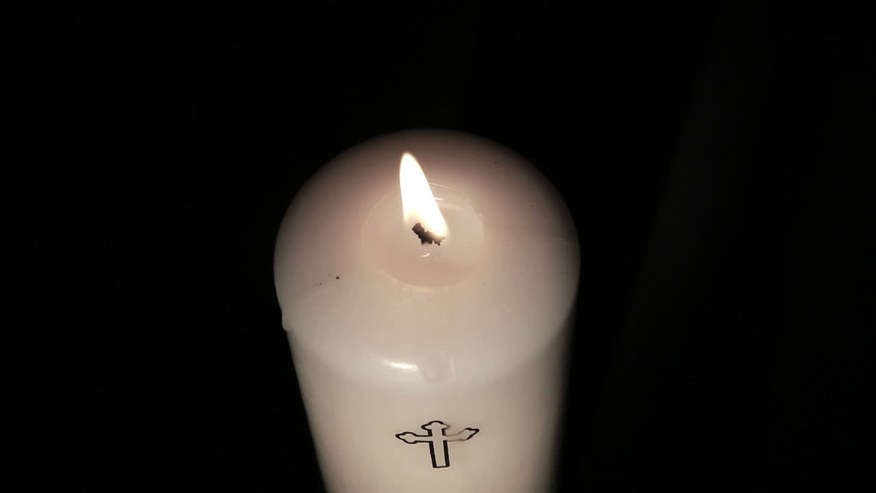 Candle with cross embellishment burning and being blown out
