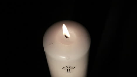 candle with cross embellishment burning and being blown out