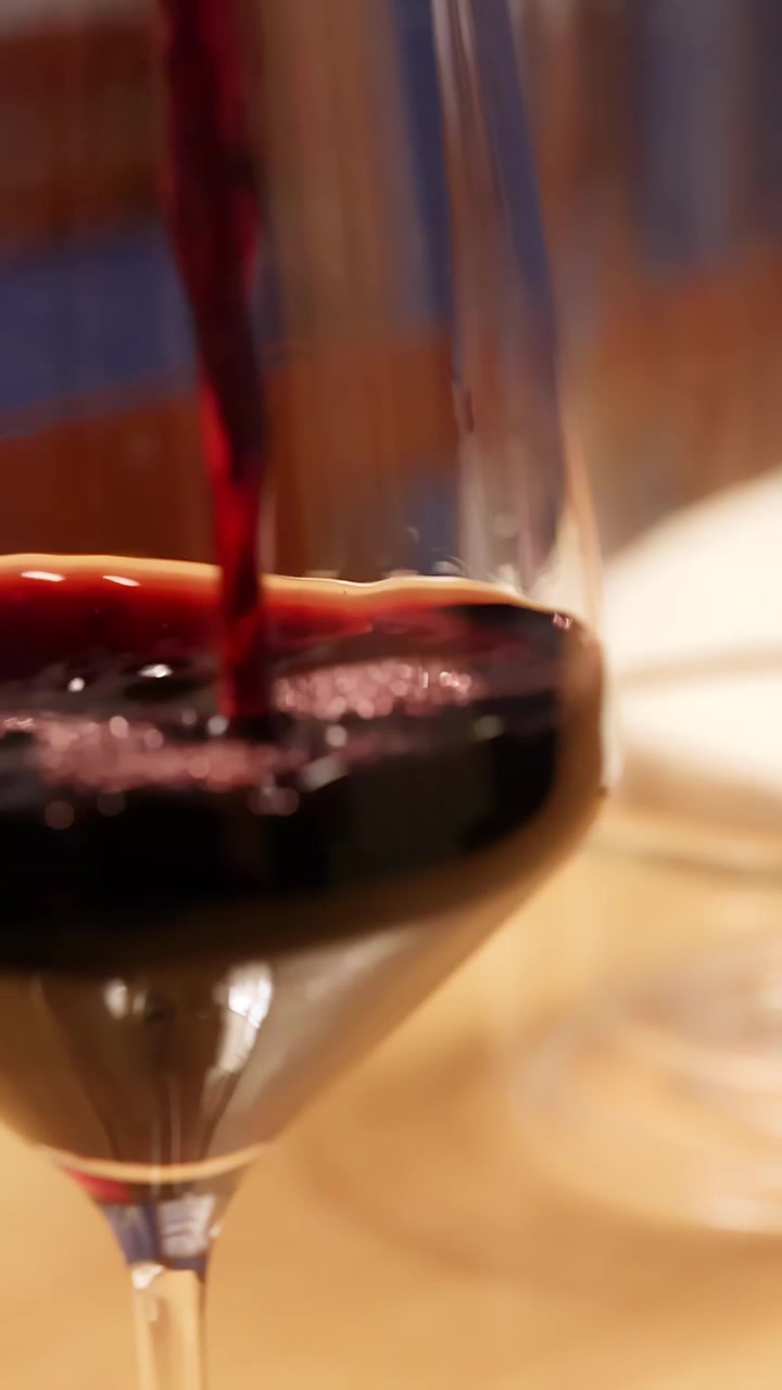 Primo piano di vino rosso che riempie un bicchiere di cristallo in un ambiente di ristorante caldo e di lusso