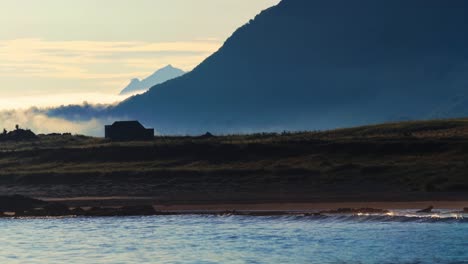 afternoon sea fog time lapse. silhouette of a house on a small island among the mountains by the sea on a warm summer afternoon. lofoten islands, northern norway