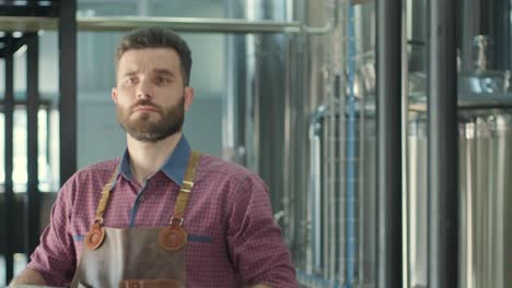 young brewer wearing a leather apron carries a barrel of craft beer at a modern brewery