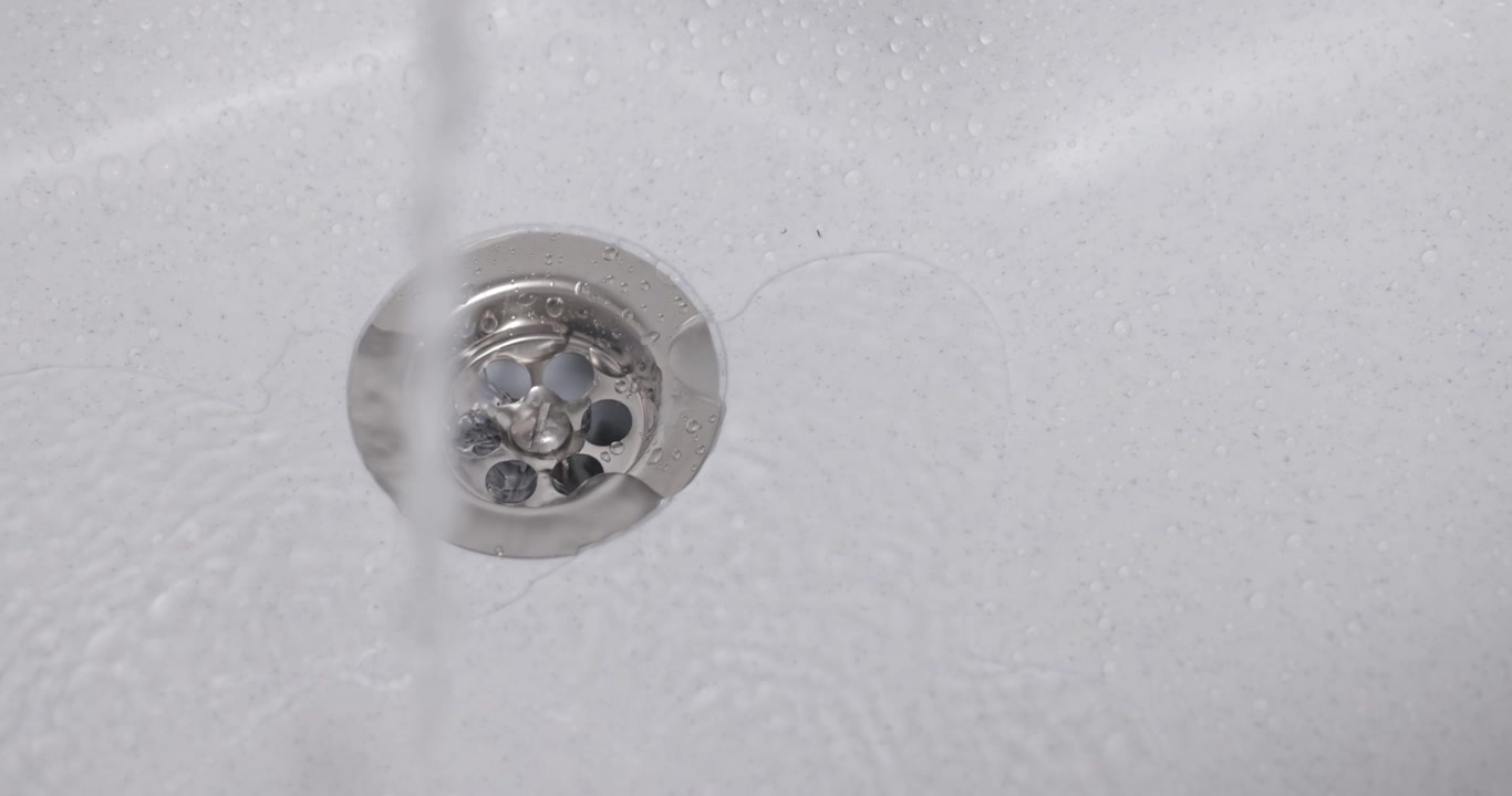 Close-up of a grey plastic sink with running water and a draining plug, 4K