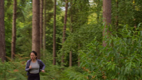 mid adult woman exercising doing work out outdoors running along track through forest towards camera wearing sports clothing 1