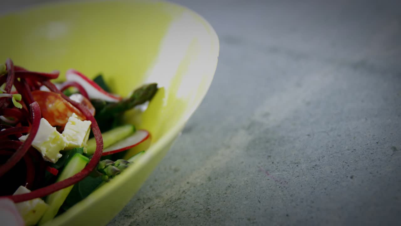 Camera tightening and green shapes drifting revealing salad detail in yellow bowl to show freshness