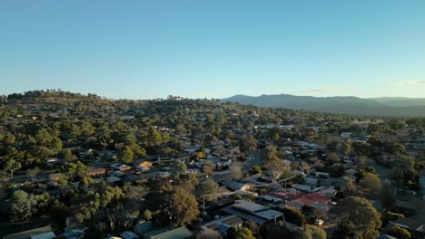 drone flies forward above suburban rooftops with the majestic brindabella mountains glowing in late afternoon light