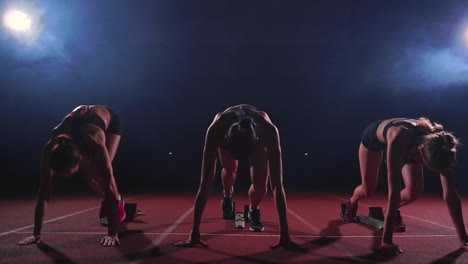 female runners at athletics track crouching at the starting blocks before a race. in slow motion.