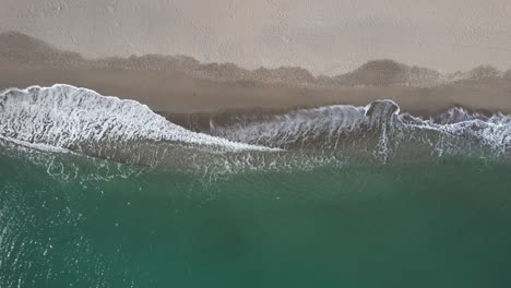 Aerial-lookdown-of-soothing-aqua-blue-sea-waves-hitting-beach-sand-drone-view