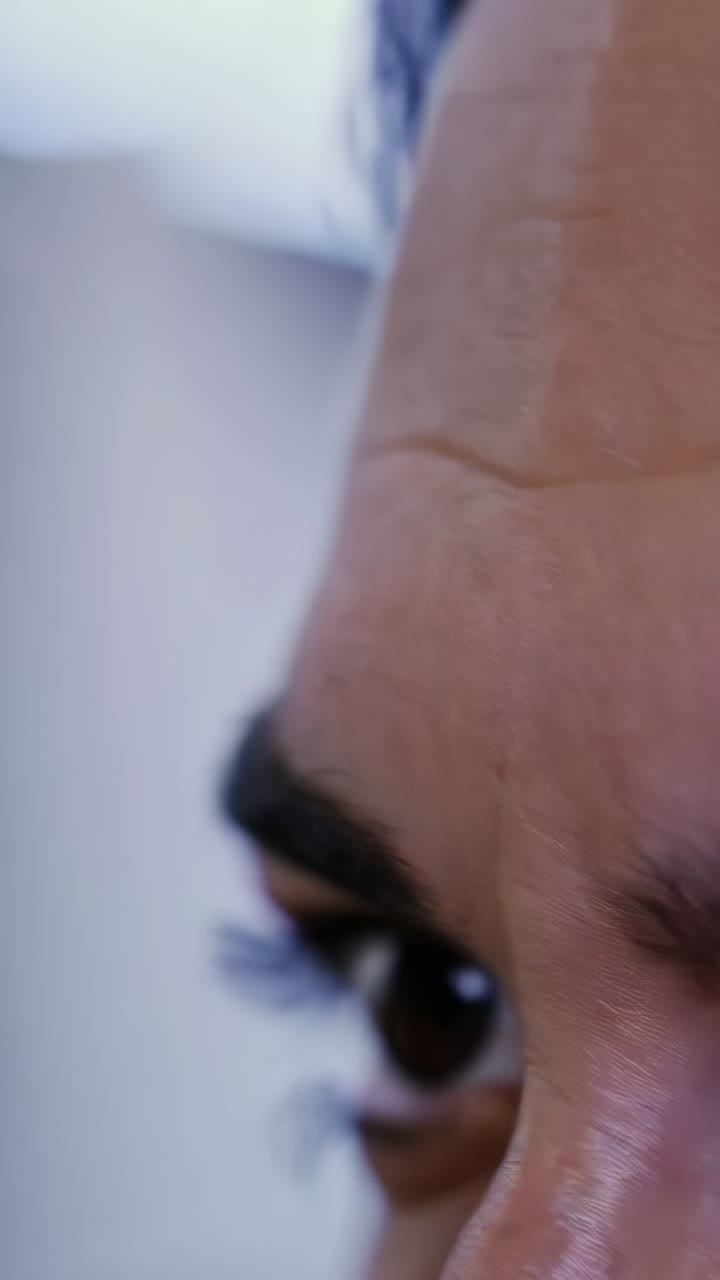 Close-up of a person's face and eye, and a hand touching the forehead.