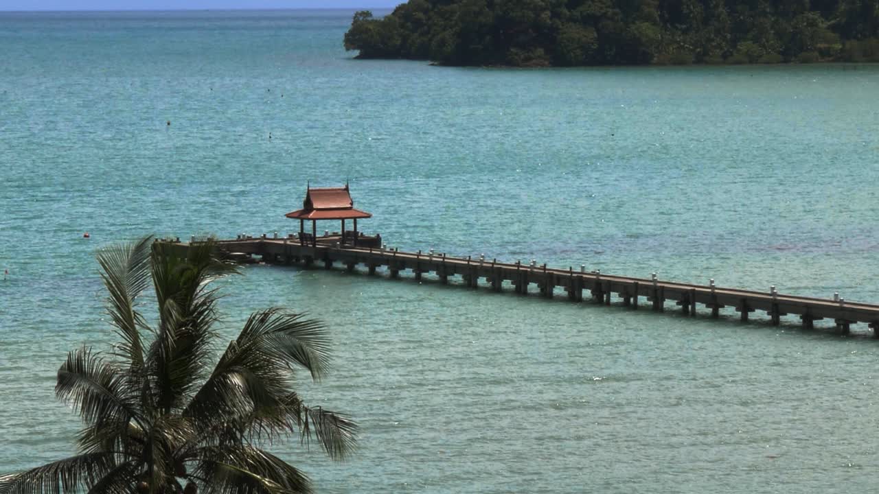 끝에 작은 빨간 지붕이 있는 부두 야자수가 있는 바다 속 crop slowmo
