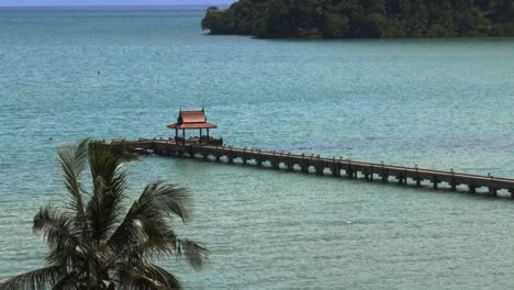 un muelle con un pequeño techo rojo al final, en el océano con cultivos de palmeras a cámara lenta