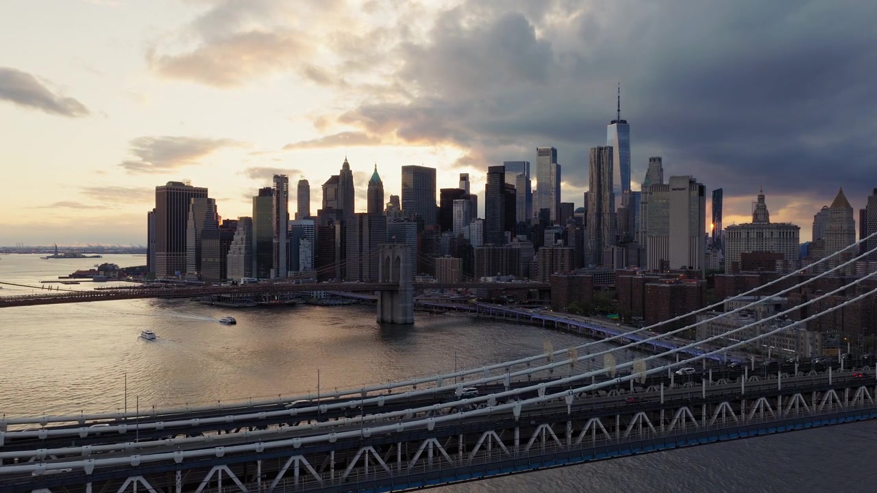 Drone panoramico vola sopra il Ponte di Manhattan verso il Ponte di Brooklyn al tramonto, New York City. Skyline di Manhattan, One World Trade Center visibile. Cielo nuvoloso dorato