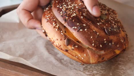 close-up view of a delicious cheese and seed bun being held by a hand