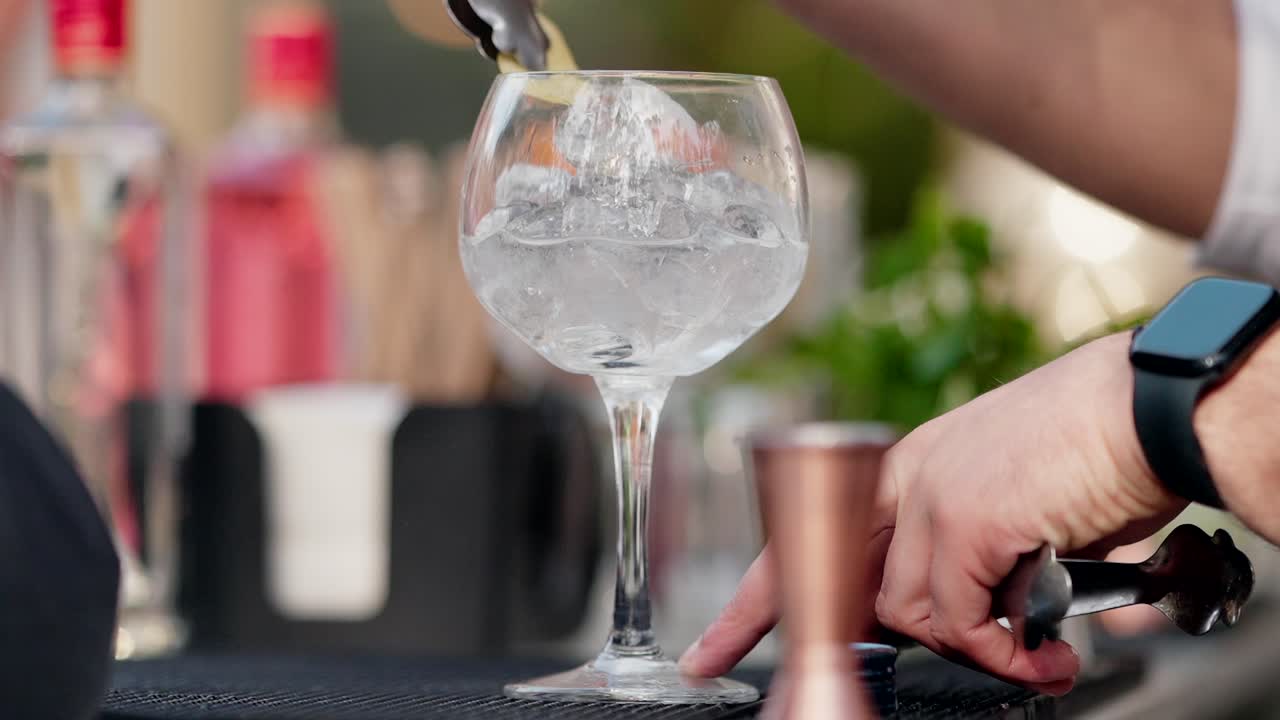 Close up of cocktail glass with ice cubes at bar surrounded by mixers and tools