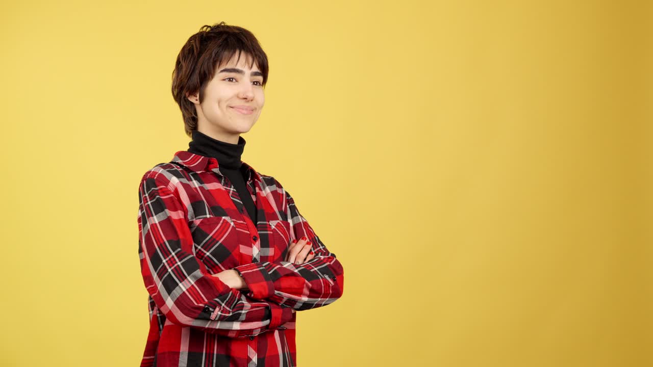 Young woman with short hair and plaid shirt smiling against a yellow background
