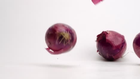 cebollas rojas enteras moradas frescas cayendo y rebotando sobre una mesa blanca a cámara lenta con capas de piel de cebolla que se desprenden