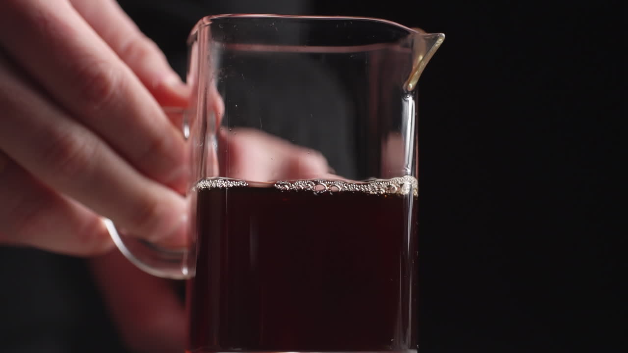 persona que sostiene una jarra de vidrio de líquido oscuro