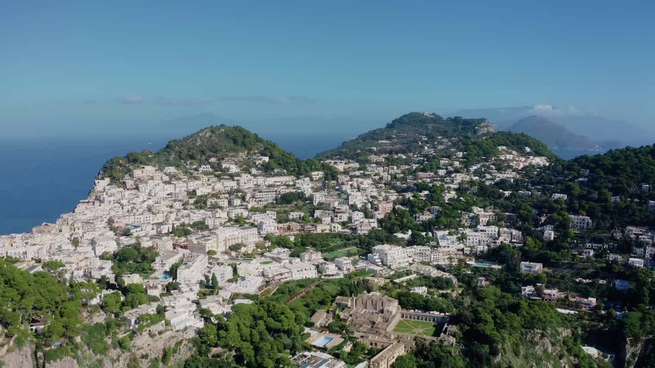 Veduta aerea con drone della città dell'isola di Capri, con edifici bianchi arroccati sulla collina, situata su un'isola rocciosa calcarea nel Mar Mediterraneo. Destinazione di viaggio estiva di lusso in Italia con paesaggio di scogliere rocciose.