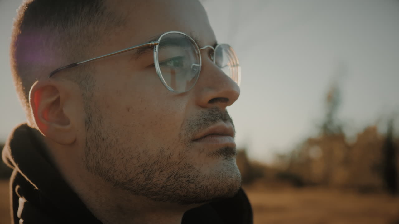 inspirado joven caucásico con gafas respirando aire fresco en la naturaleza al atardecer o al amanecer