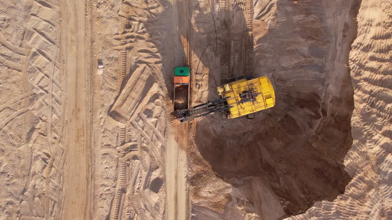 Electric rope shovel on sand mining in opencast. Mining excavator dropping rock ore into mine dump truck.