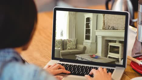 mujer usando una computadora portátil con interiores de sala de estar modernos mostrados en la pantalla