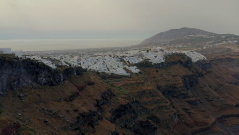 Antena:-Dron-Panorámico-Lento-Tomado-De-Fira-En-Santorini,-Grecia-Durante-El-Amanecer-Nublado