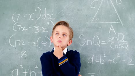 Thoughtful-schoolboy-standing-in-front-of-chalkboard