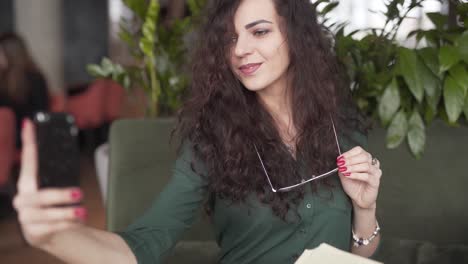 Eine-Schöne-Junge-Frau-Macht-Ein-Paar-Selfies,-Während-Sie-Mit-Ihrer-Brille-In-Einem-Café-Posiert