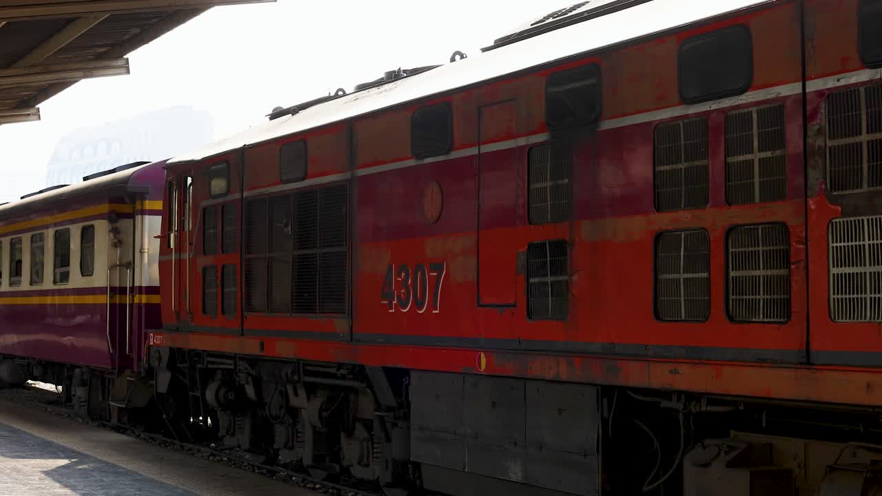 Side view of vintage red diesel locomotive pulling passenger carriages past platform, handheld daylight shot