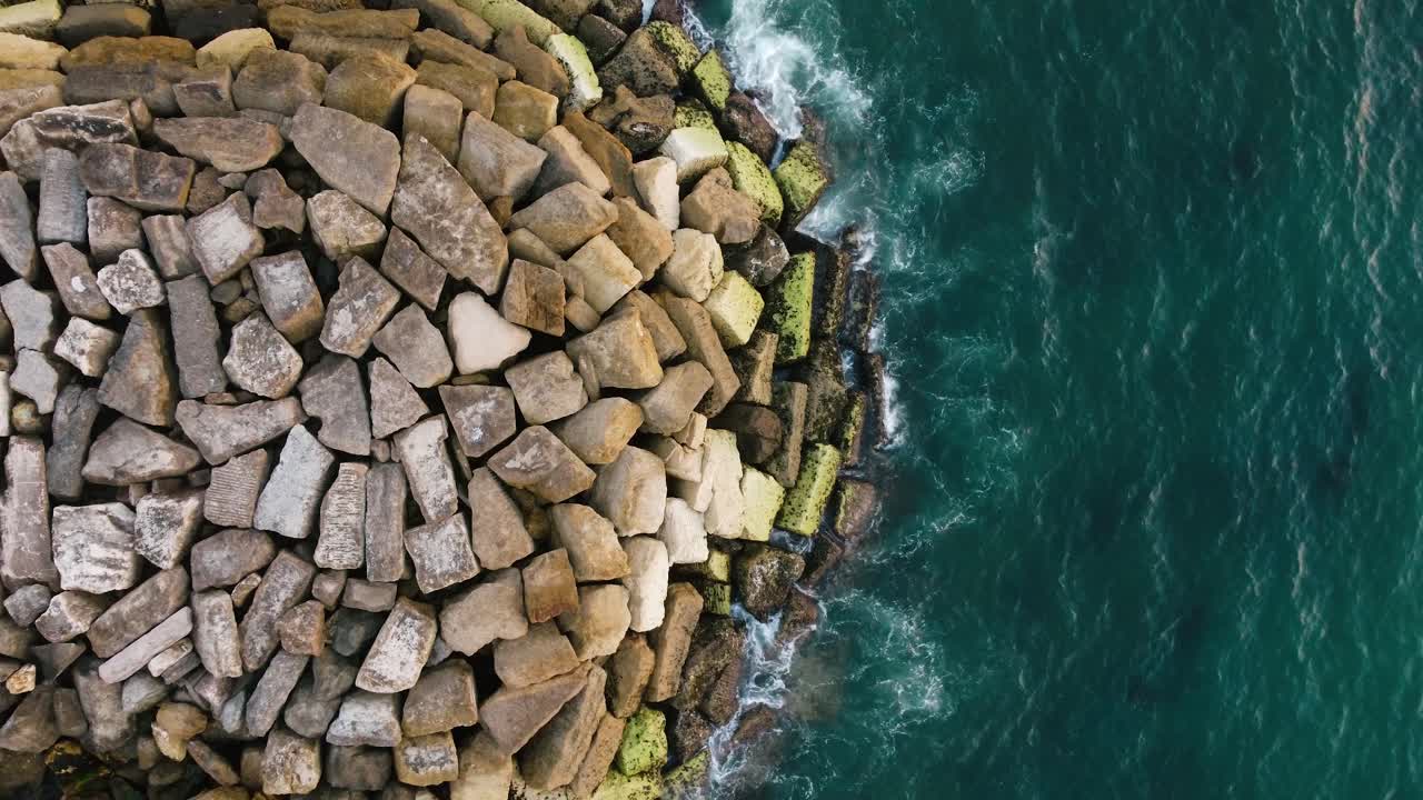 Fugleperspektiv af små bølger, der bryder mod klippetoppe i det blå hav, Ericeira, Portugal
