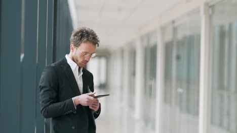 Handsome-man-in-a-business-suit-standing-in-the-hallway-with-a-tablet