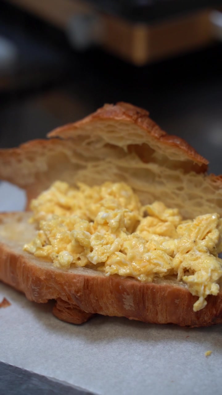 Preparazione di una deliziosa colazione mattutina. Uno chef dosa con cura uova strapazzate cremose in un croissant francese sfogliato su carta da forno.